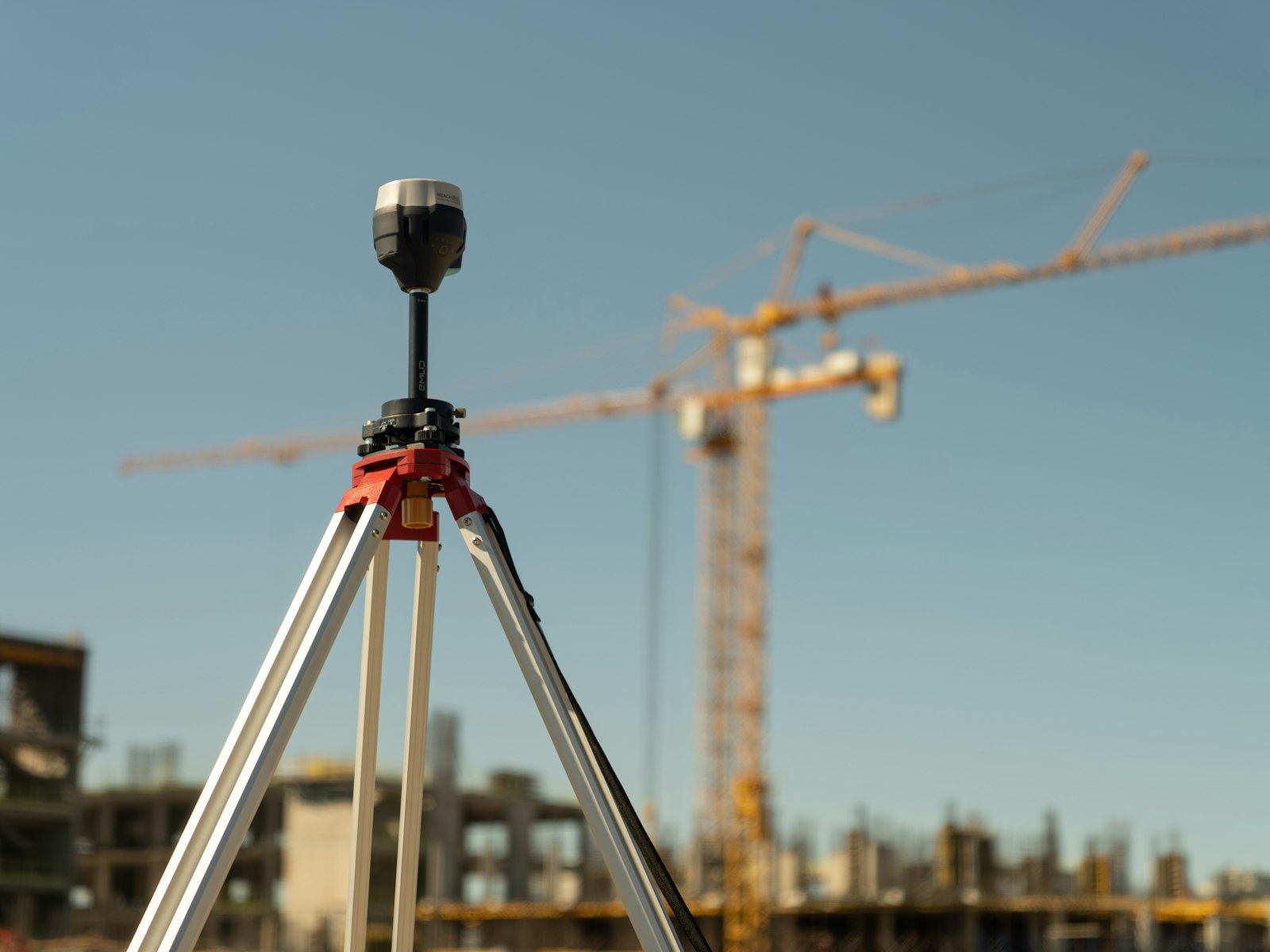 A survey instrument on a tripod in front of a construction site