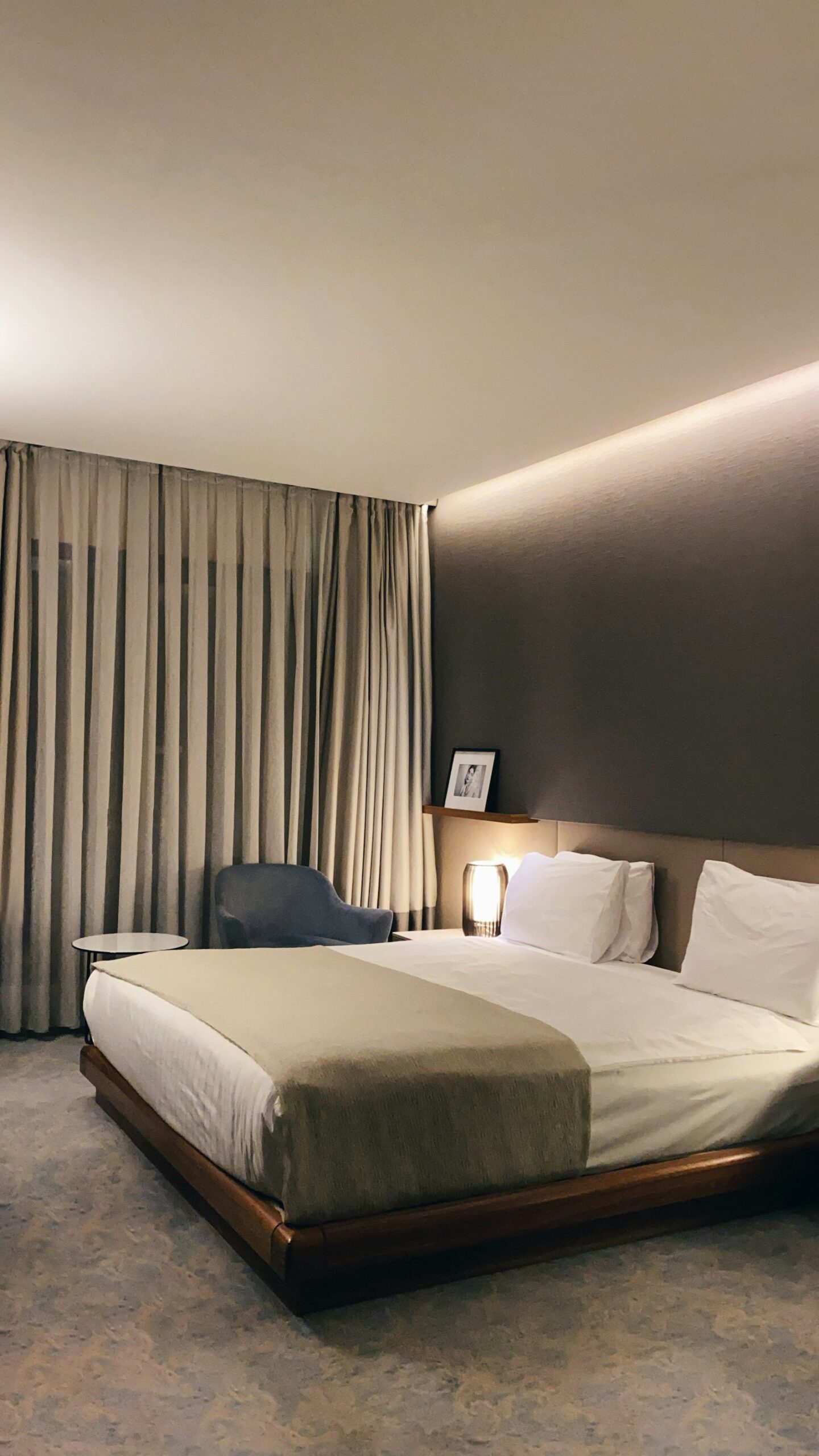 A made-up hotel bed with a grey pillow beside a window